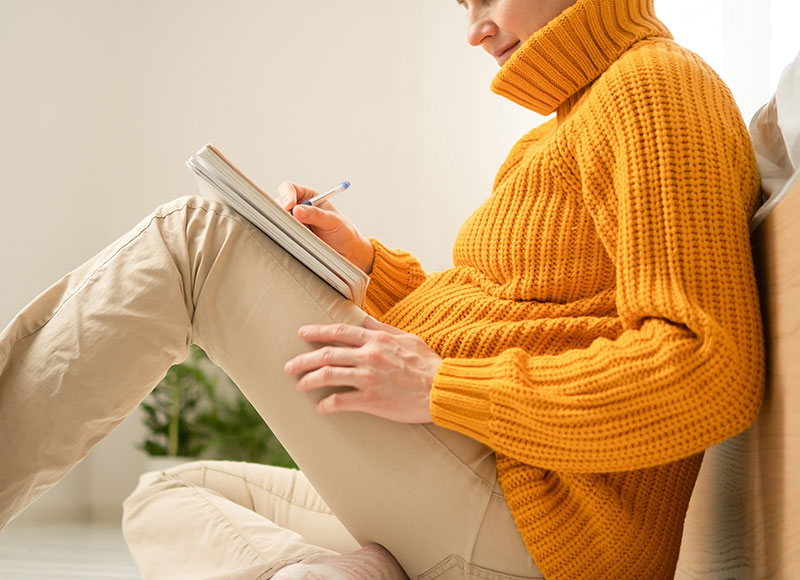 A new parent sitting comfortably and writing in a planner, using quiet planning time to stay organized during the newborn stage.