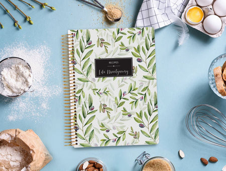 A Posy Paper Co. recipe book on a kitchen counter with baking ingredients ready to capture your favorite moments in the kitchen.