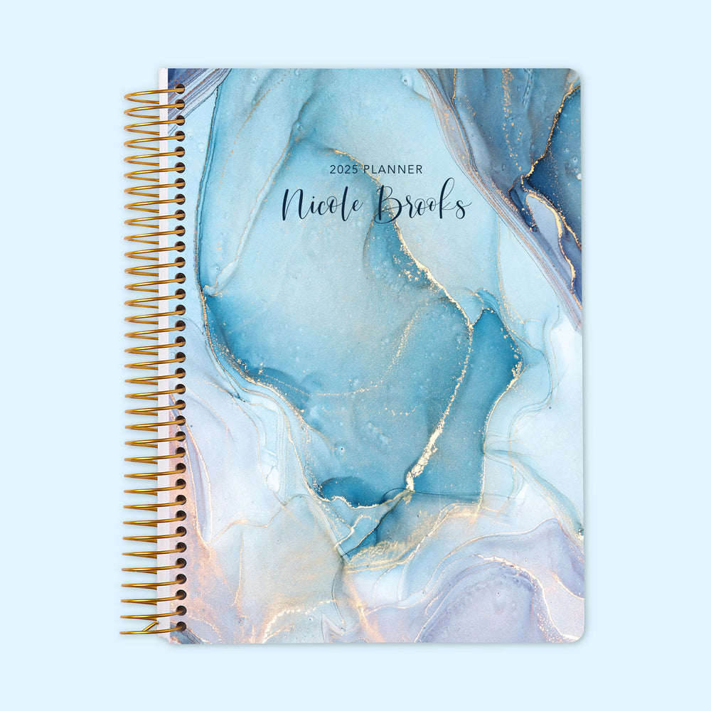 Monthly planner featuring an aqua and gold ink swirl design, mimicking fluid art with a modern metallic touch, bound with a sturdy coil.