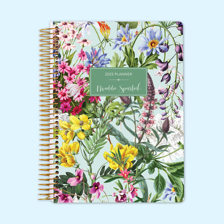 Monthly planner featuring lively green floral accents on a light backdrop, blending soft painted details with a natural aesthetic, bound with a sturdy coil.