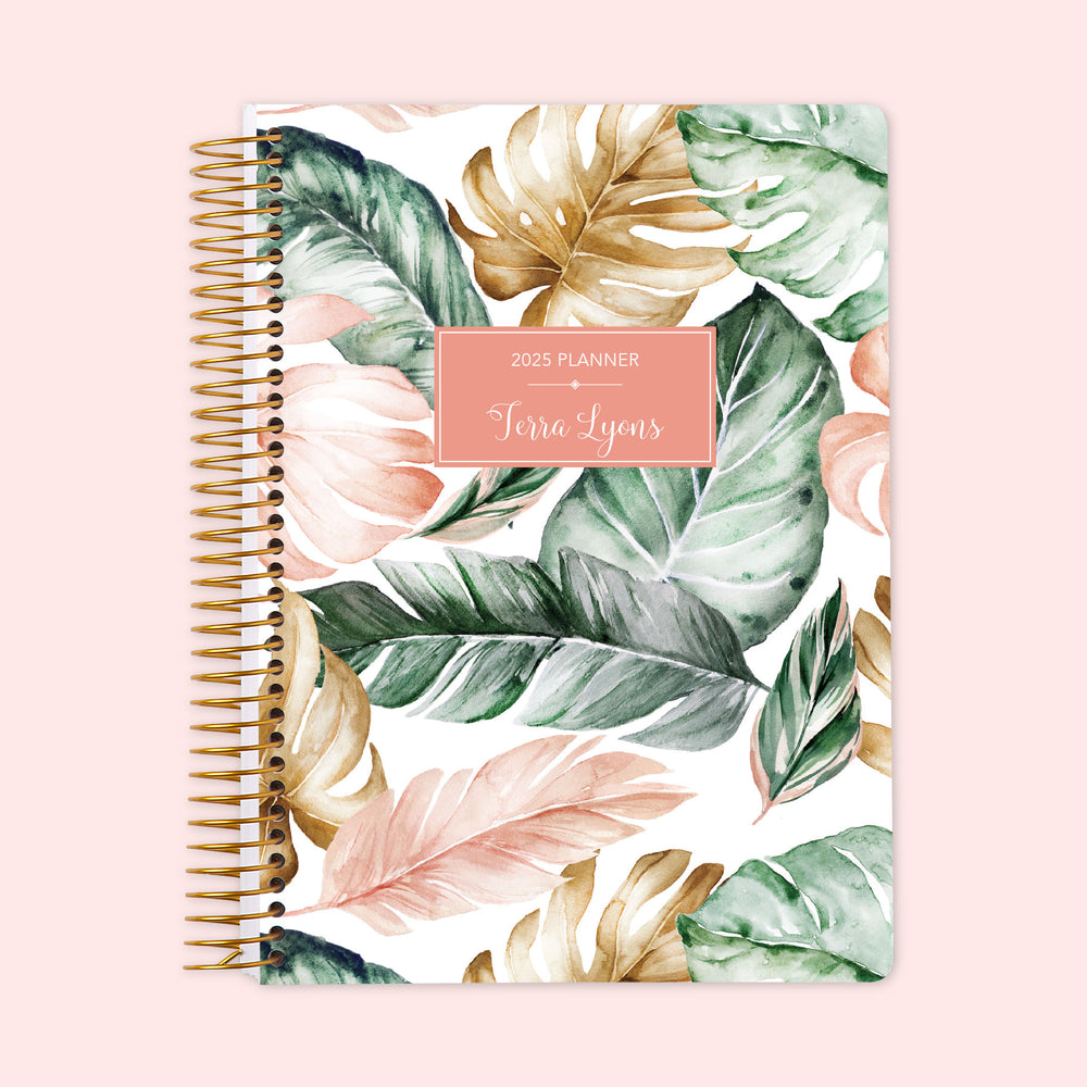 Weekly planner featuring a chic blush and gold tropical cover, decorated with palm leaves and gold accents, protected by a durable spiral binding and customizable with your name for organized planning with a vacation vibe.