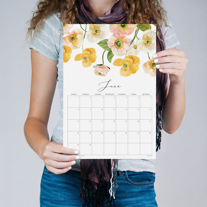 Person holding the June Flirty Florals wall calendar with yellow floral artwork