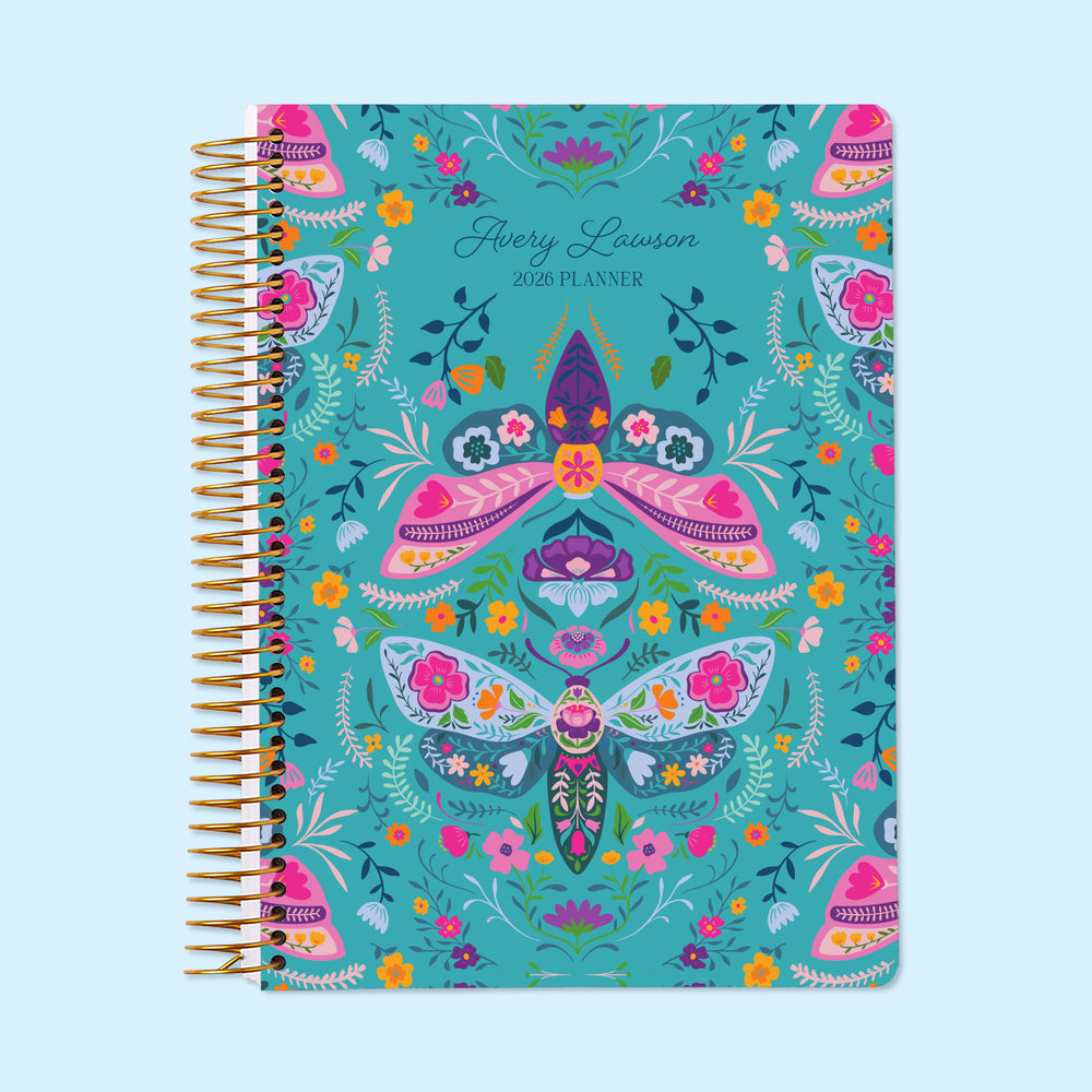 6×9 Meadow Daybreak Wings personalized monthly planner with customizable start month, gold coil binding, and a whimsical teal floral cover featuring illustrated moths, butterflies, and garden accents.