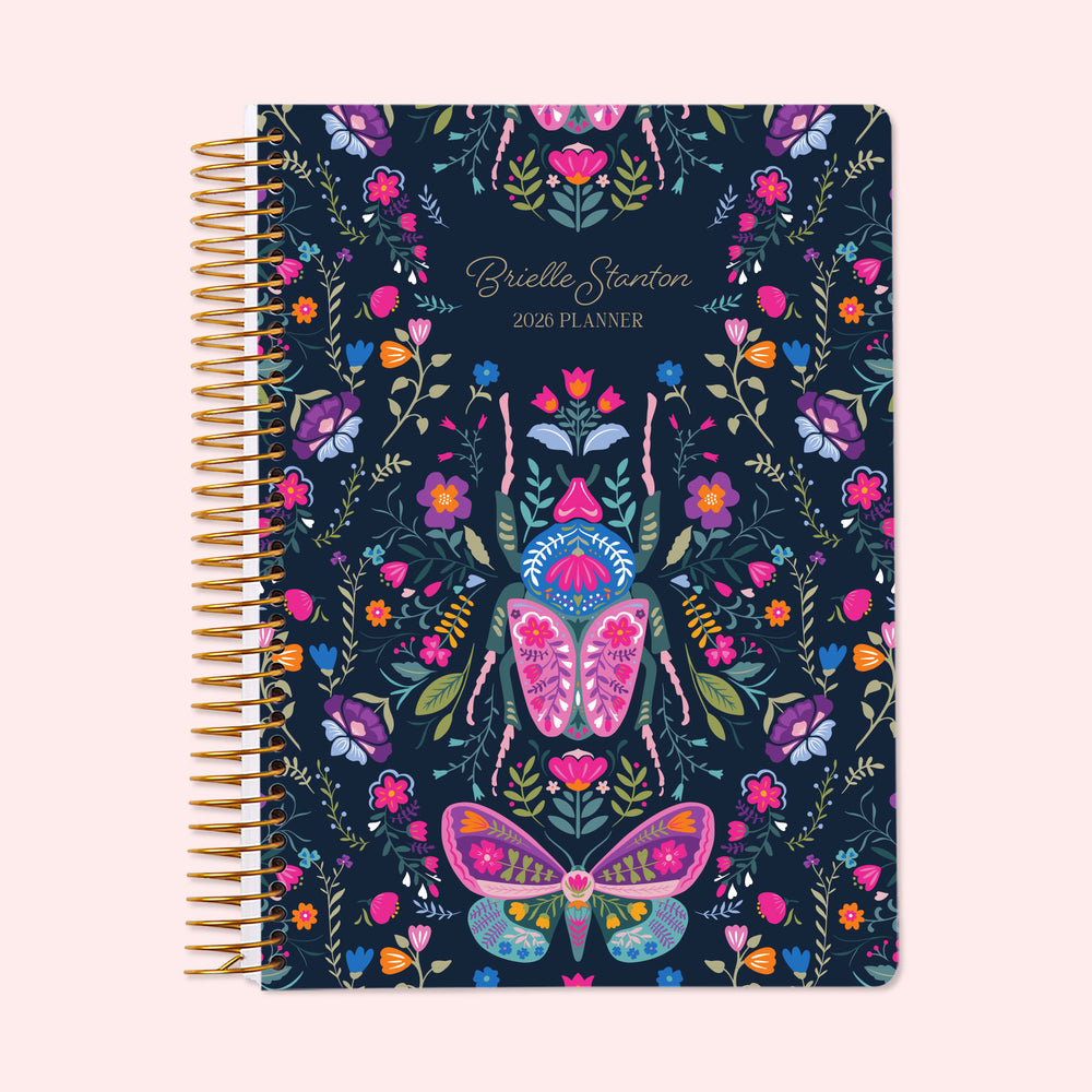 6×9 Midnight Garden Wings personalized weekly planner with flexible start month, gold coil binding, and a deep navy floral cover featuring colorful butterflies, moths, and stylized garden botanicals.
