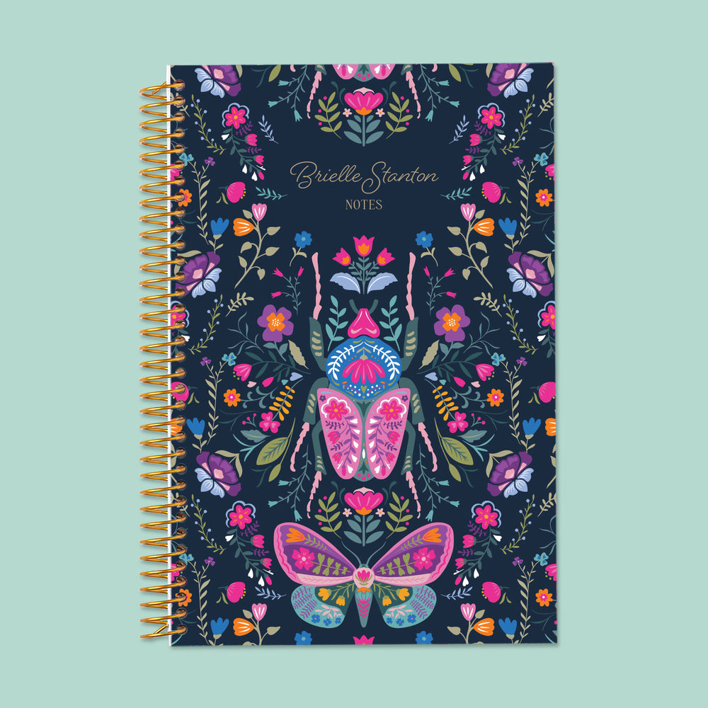 Midnight Garden Wings personalized notebook with optional name customization, gold coil binding, and a deep navy floral cover featuring illustrated butterflies, moths, and vibrant garden botanicals.