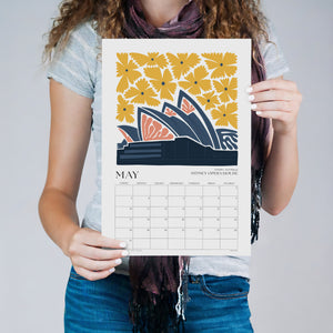 
                  
                    Person holding the May travel wall calendar with a Sydney Opera House illustration
                  
                