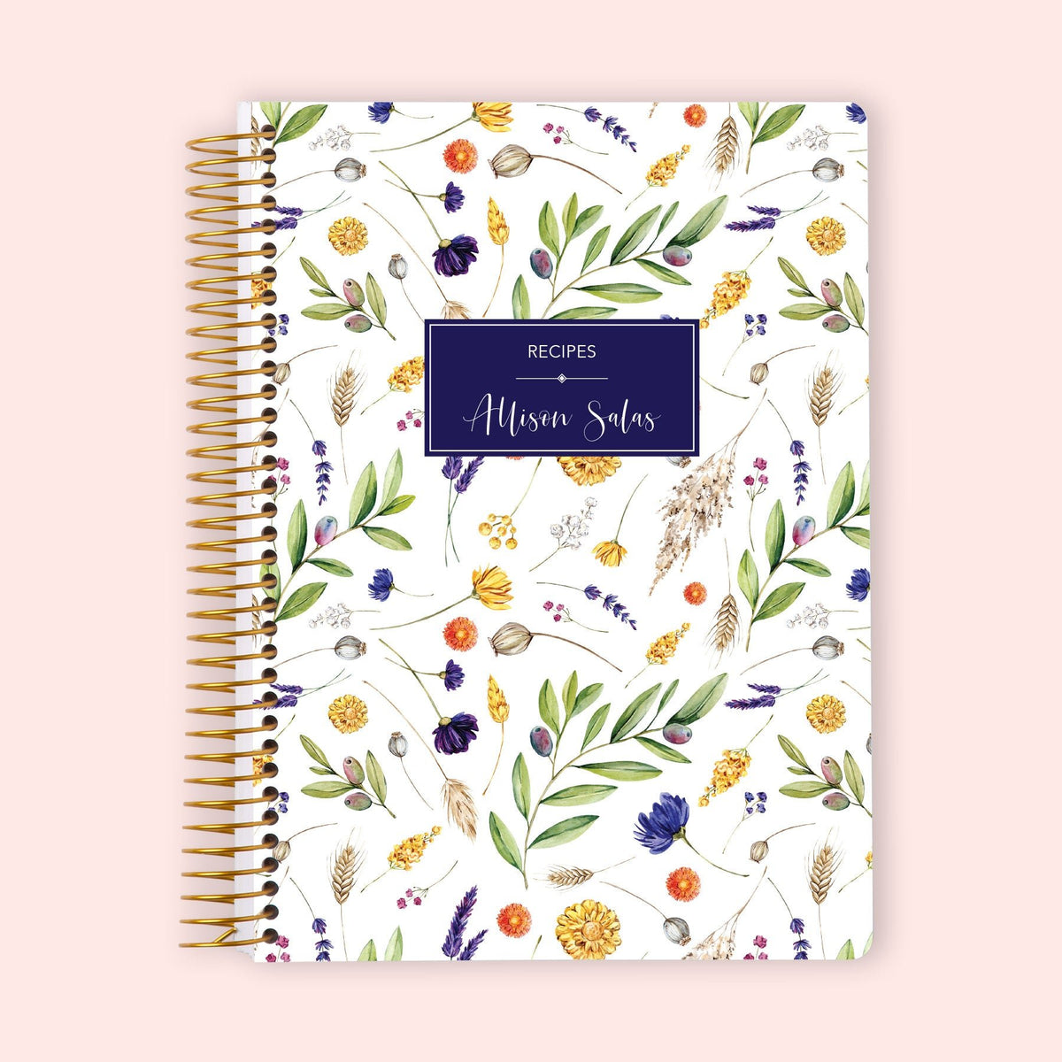 Recipe book with a personalized navy label, yellow and purple botanical cover and gold coil binding.