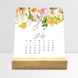
                  
                    July Flirty Florals desk calendar card with watercolor flowers in a wooden stand.
                  
                